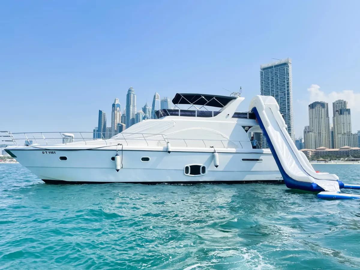 Yacht vor der Skyline der Dubai Marina mit einer aufblasbaren Wasserrutsche ins Meer